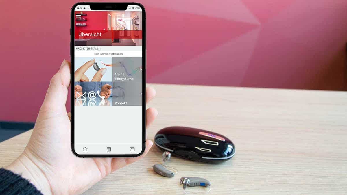 Eine Hand hält ein Smartphone, daneben liegen Hörgeräte und das Hörgeräte Etui. Der Bildschirm des Smartphones zeigt die zu den Hörgeräten passende App und die Einstellung des Musikprogramms für perfekten Musikgenuss mit Hörgeräten